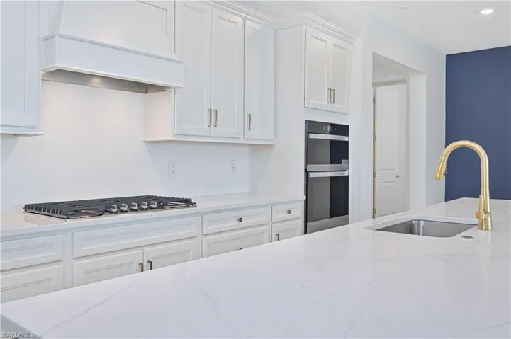 Kitchen featuring light stone counters, white cabinets, and custom range hood