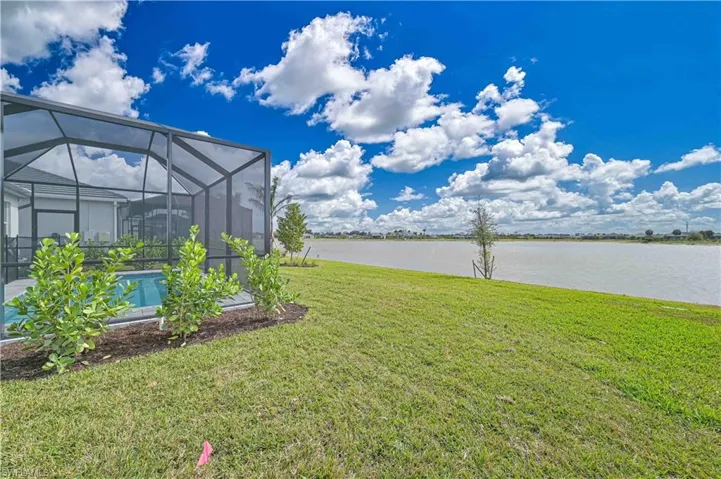 View of grassy yard with a lanai, a water view, a sunroom, and an outdoor pool