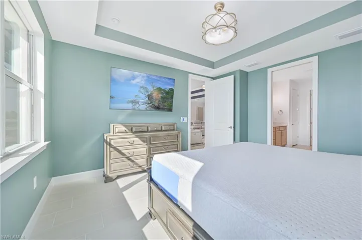Bedroom featuring a raised ceiling, light tile patterned floors, and ensuite bath
