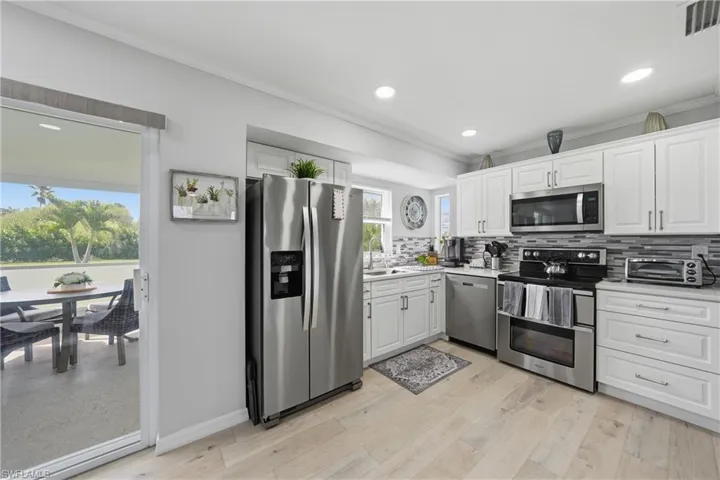 Kitchen with ornamental molding, stainless steel appliances, white cabinetry, backsplash, and light wood-style flooring
