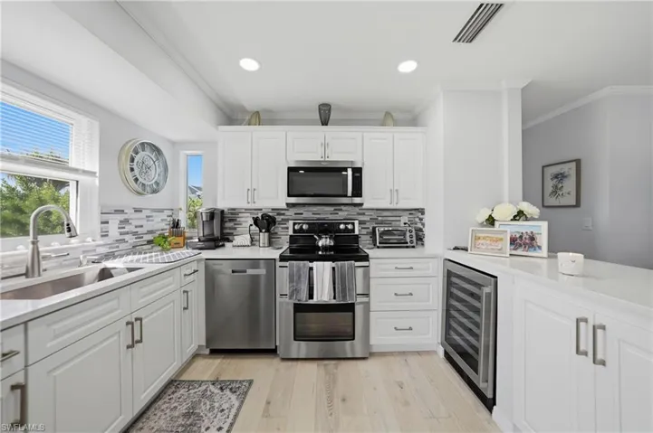 Kitchen with white cabinetry, stainless steel appliances, light wood-style flooring, beverage cooler, and light stone counters