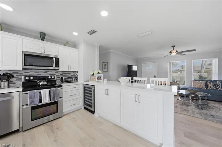 Kitchen featuring a peninsula, stainless steel appliances, a breakfast bar area, crown molding, and white cabinetry