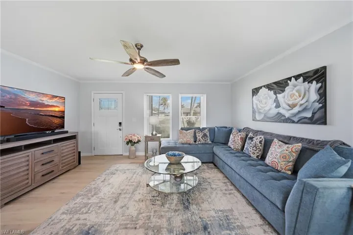 Living room with light wood-style flooring, a ceiling fan, and ornamental molding