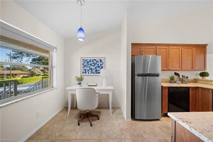 Kitchen featuring freestanding refrigerator, brown cabinetry, dishwasher, and light stone counters