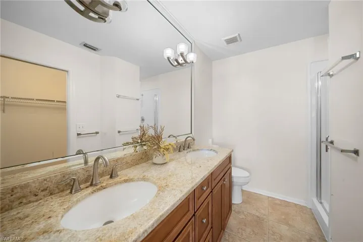 Bathroom with double vanity, a spacious closet, a shower stall, light tile patterned floors, and a chandelier