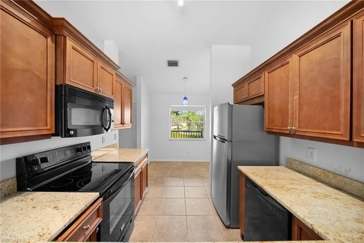 Kitchen with black appliances, hanging light fixtures, light stone counters, brown cabinetry, and light tile patterned flooring
