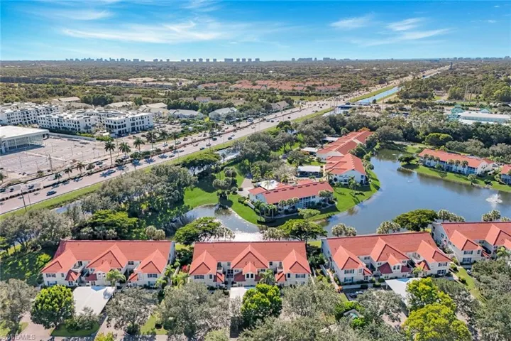 Aerial view of multi-unit residential buildings featuring red tile roofs, stucco exteriors, waterfront positioning, and mature landscaping