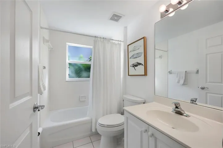 Full bathroom featuring a white vanity with an integrated basin, a large wall-mounted mirror, a tub-shower combination with tile surround, and tile flooring