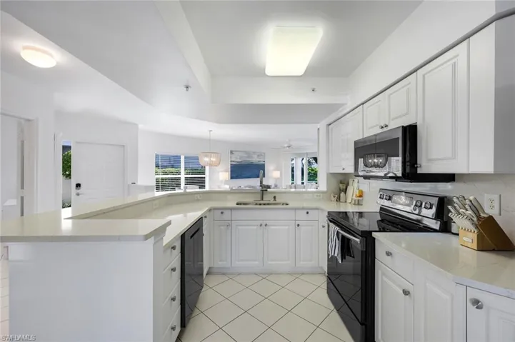 Kitchen featuring white shaker-style cabinetry, solid-surface countertops, black appliances, a double-basin undermount sink, and tile flooring