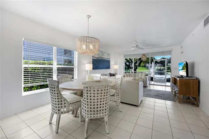 Open-concept interior featuring large-format ceramic tile flooring, a tiered beaded chandelier, expansive windows, a ceiling fan, and sliding glass doors with exterior patio access