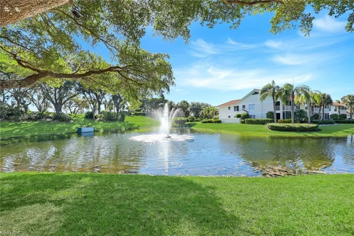 Water feature centered in a pond, surrounded by manicured lawn, mature trees, and palm vegetation