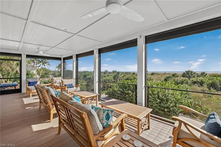 Sunroom featuring a ceiling fan, expansive windows, an outdoor hangout area, and view of scattered trees