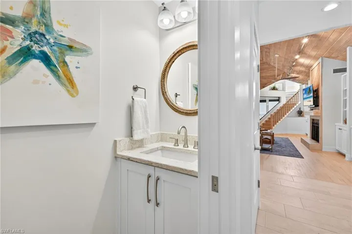 Half bath featuring vanity, vaulted ceiling, light wood finished floors, wood ceiling, and a fireplace with raised hearth