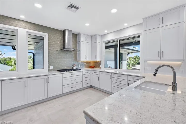 Kitchen with light stone countertops, recessed lighting, tasteful backsplash, wall chimney exhaust hood, and white cabinets