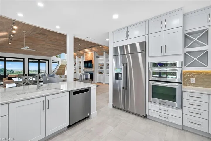 Kitchen with light stone countertops, appliances with stainless steel finishes, a ceiling fan, wood ceiling, and open floor plan