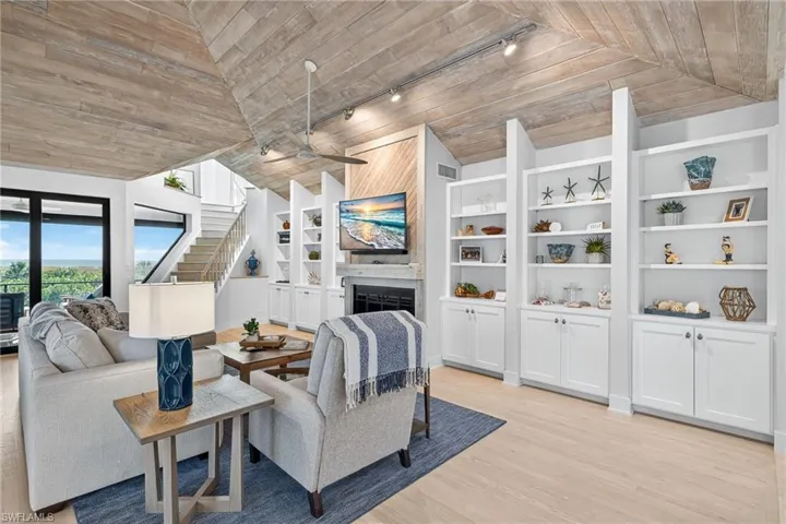 Living room featuring a fireplace, track lighting, built in features, light wood-style floors, and lofted ceiling