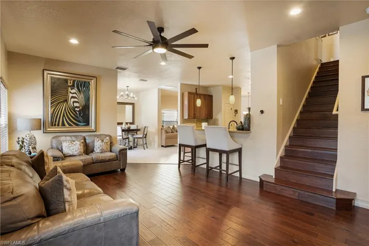 Living area featuring recessed lighting, ceiling fan with notable chandelier, dark wood-type flooring, visible vents, and stairs