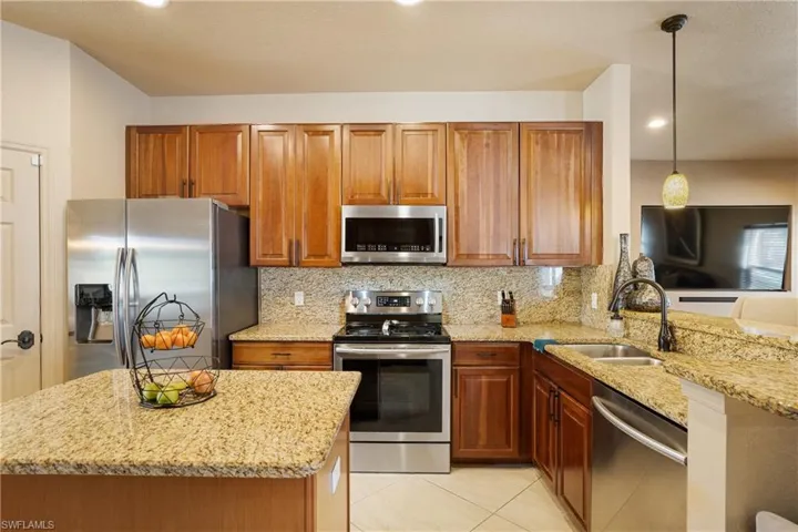 Kitchen with light stone counters, pendant lighting, appliances with stainless steel finishes, brown cabinetry, and a sink
