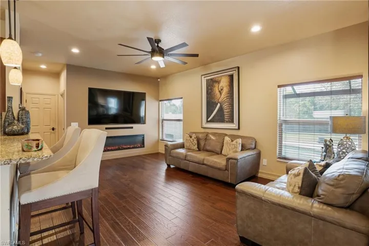 Living room with baseboards, a glass covered fireplace, dark wood finished floors, and recessed lighting