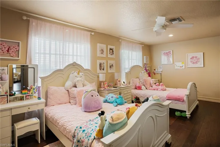 Bedroom featuring a textured ceiling, visible vents, baseboards, a ceiling fan, and dark wood finished floors