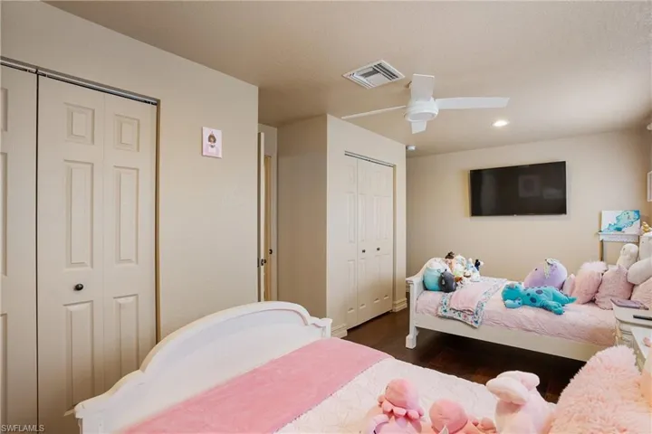 Bedroom with a textured ceiling, a ceiling fan, visible vents, multiple closets, and dark wood-style floors