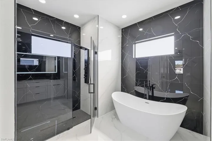 Bathroom with a soaking tub, marble tiled floors, a marble finish shower, stone wall, and tile walls
