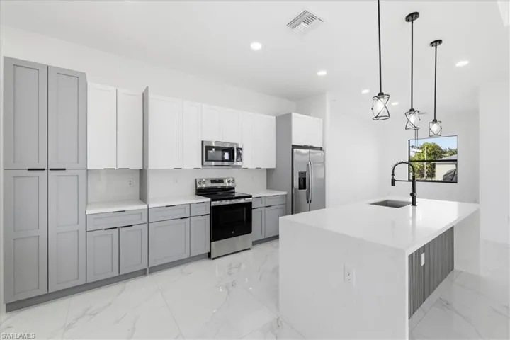 Kitchen featuring stainless steel appliances, pendant lighting, gray cabinets, light marble finish flooring, and recessed lighting