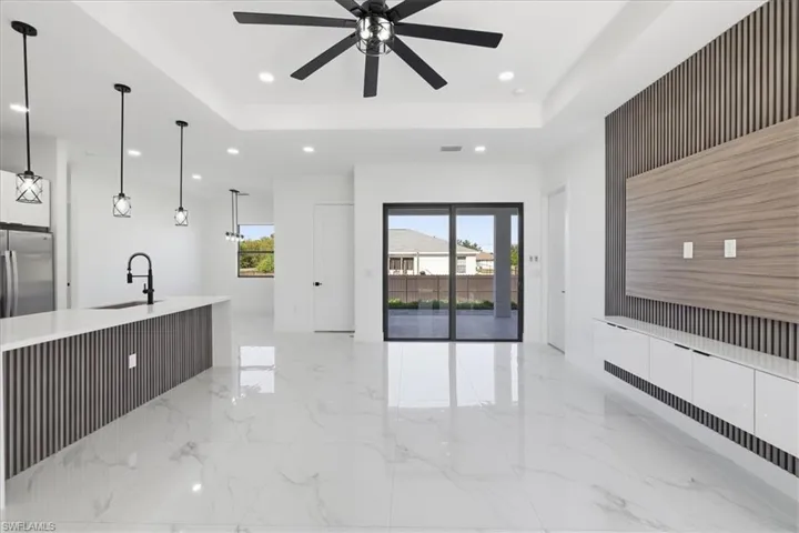 Kitchen with a tray ceiling, decorative light fixtures, recessed lighting, light marble finish floors, and light stone counters