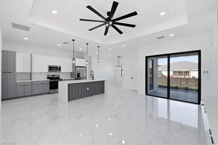 Kitchen featuring a raised ceiling, recessed lighting, gray cabinets, stainless steel appliances, and a center island with sink
