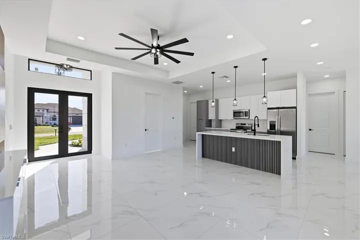 Kitchen with open floor plan, a center island with sink, white cabinetry, decorative light fixtures, and light marble finish flooring