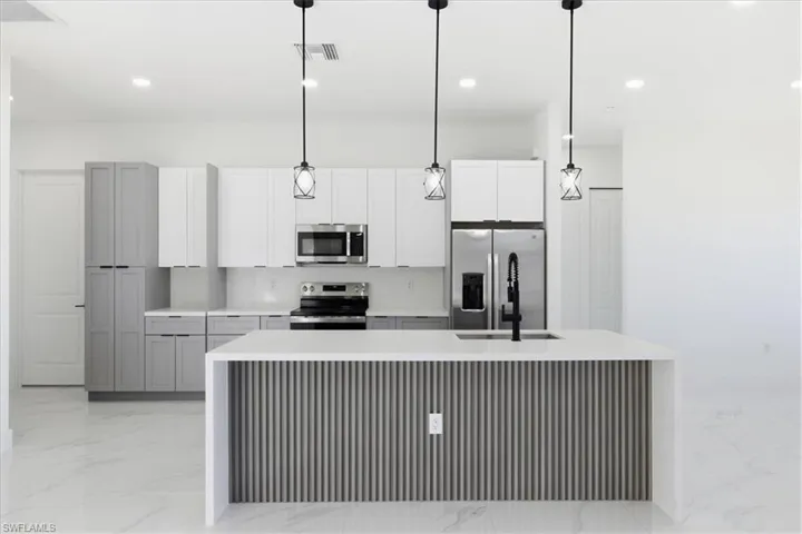 Kitchen featuring stainless steel appliances, light stone countertops, pendant lighting, an island with sink, and recessed lighting