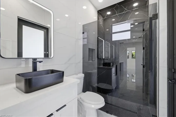 Full bathroom featuring vanity, a marble finish shower, tile walls, recessed lighting, and marble tiled floors