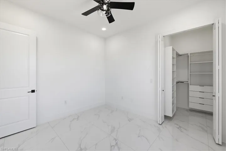 Unfurnished bedroom featuring light marble finish flooring, a walk in closet, ceiling fan, and recessed lighting