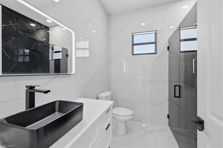 Bathroom featuring vanity, tile walls, a marble finish shower, light marble finish floors, and recessed lighting