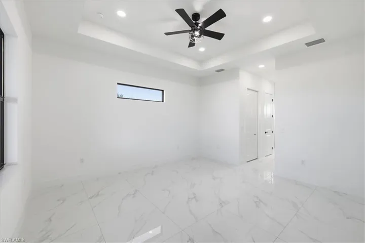 Unfurnished room with a raised ceiling, light marble finish flooring, recessed lighting, and ceiling fan