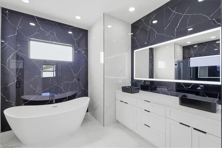 Full bath featuring a soaking tub, double vanity, stone wall, tile walls, and a marble finish shower