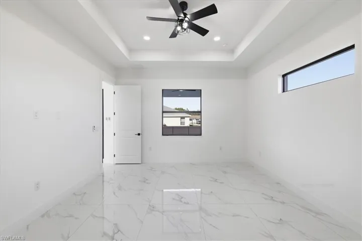 Spare room featuring light marble finish floors, a tray ceiling, a ceiling fan, and recessed lighting