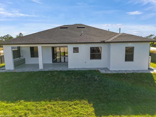 Rear view of house with a patio area, stucco siding, and a shingled roof