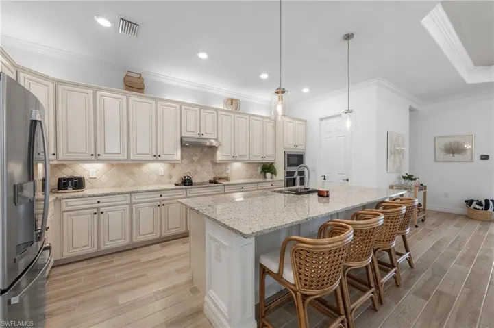 Kitchen featuring decorative light fixtures, crown molding, a kitchen breakfast bar, light stone countertops, and appliances with stainless steel finishes