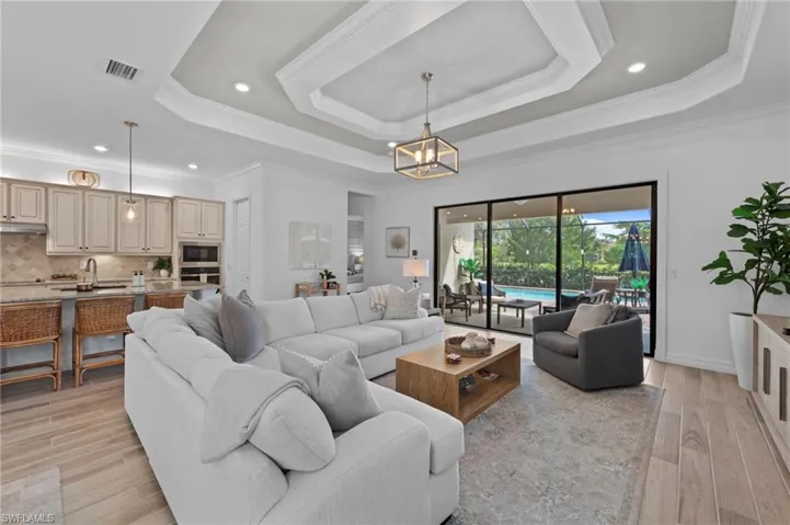Living area featuring a tray ceiling, crown molding, recessed lighting, light wood-style flooring, and a chandelier