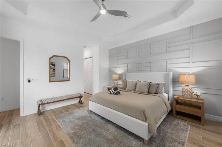Bedroom featuring wood finish floors, a raised ceiling, a closet, ornamental molding, and ceiling fan