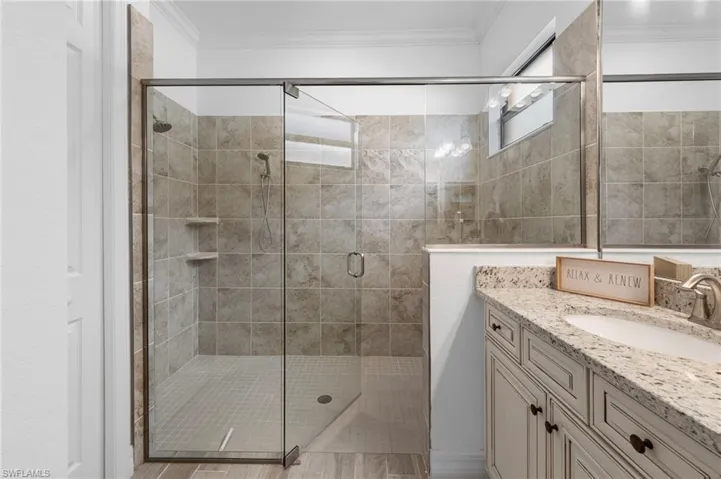 Bathroom featuring a stall shower, vanity, and crown molding
