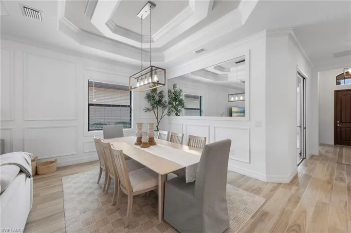 Dining area with a tray ceiling, light wood-style flooring, crown molding, a decorative wall, and healthy amount of natural light