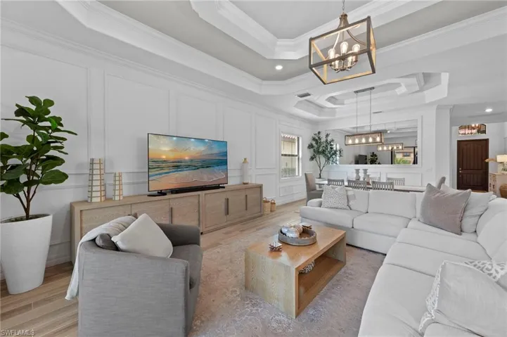 Living room featuring a raised ceiling, a decorative wall, wood finished floors, ornamental molding, and a chandelier
