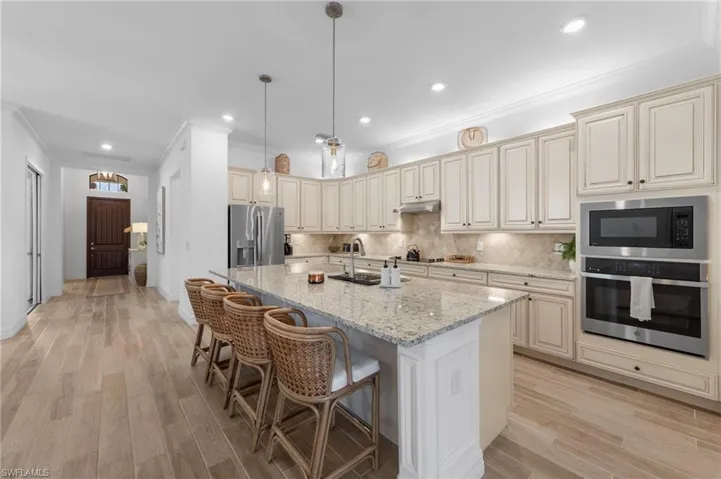 Kitchen with cream cabinetry, crown molding, appliances with stainless steel finishes, decorative backsplash, and light stone countertops