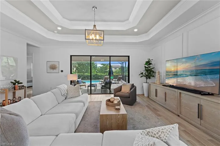 Living area featuring wood finished floors, ornamental molding, recessed lighting, a chandelier, and a raised ceiling