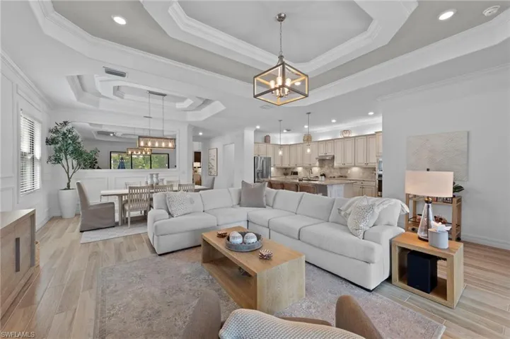 Living area with a raised ceiling, a chandelier, light wood-style floors, ornamental molding, and recessed lighting