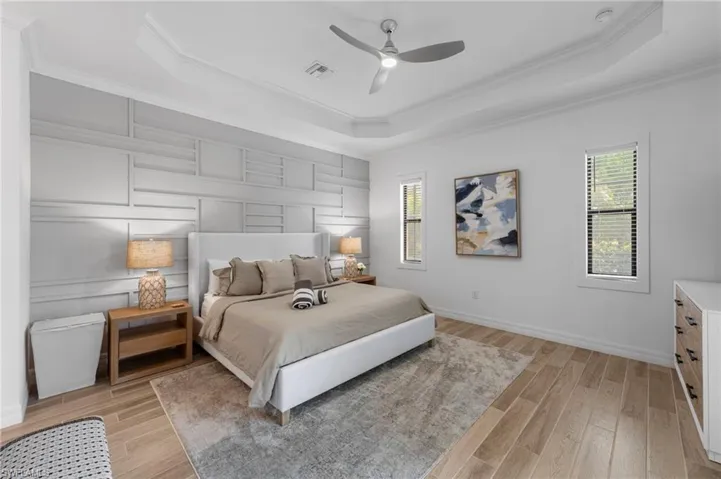 Bedroom with a raised ceiling, multiple windows, light wood finished floors, and ornamental molding