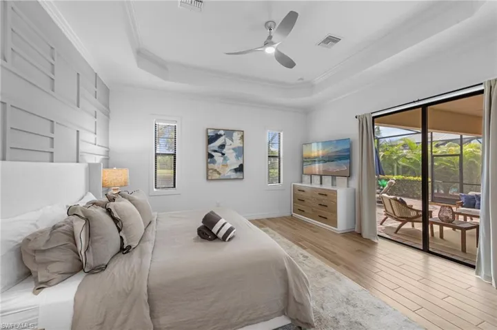 Bedroom with a tray ceiling, light wood-type flooring, crown molding, access to outside, and a ceiling fan