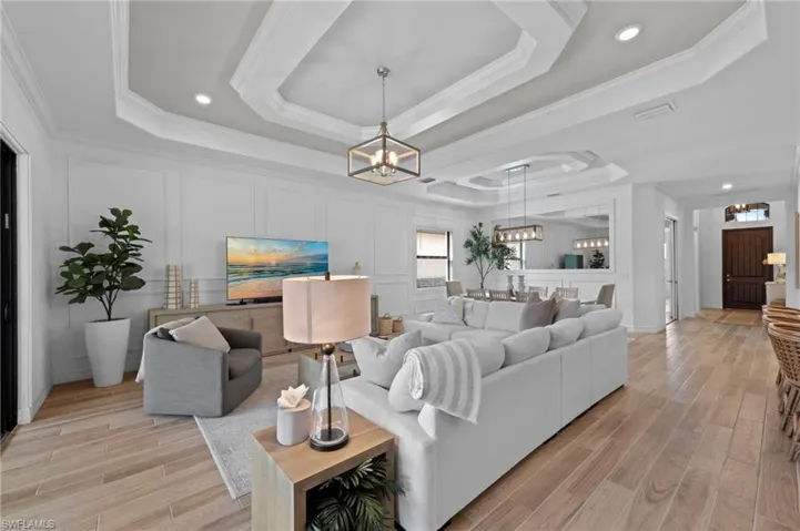 Living room featuring a tray ceiling, ornamental molding, light wood-style flooring, recessed lighting, and a chandelier